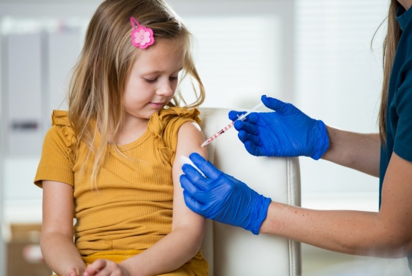 Ei junges Mädchen wird in den Arm geimpft, während sie ruhig zusieht.